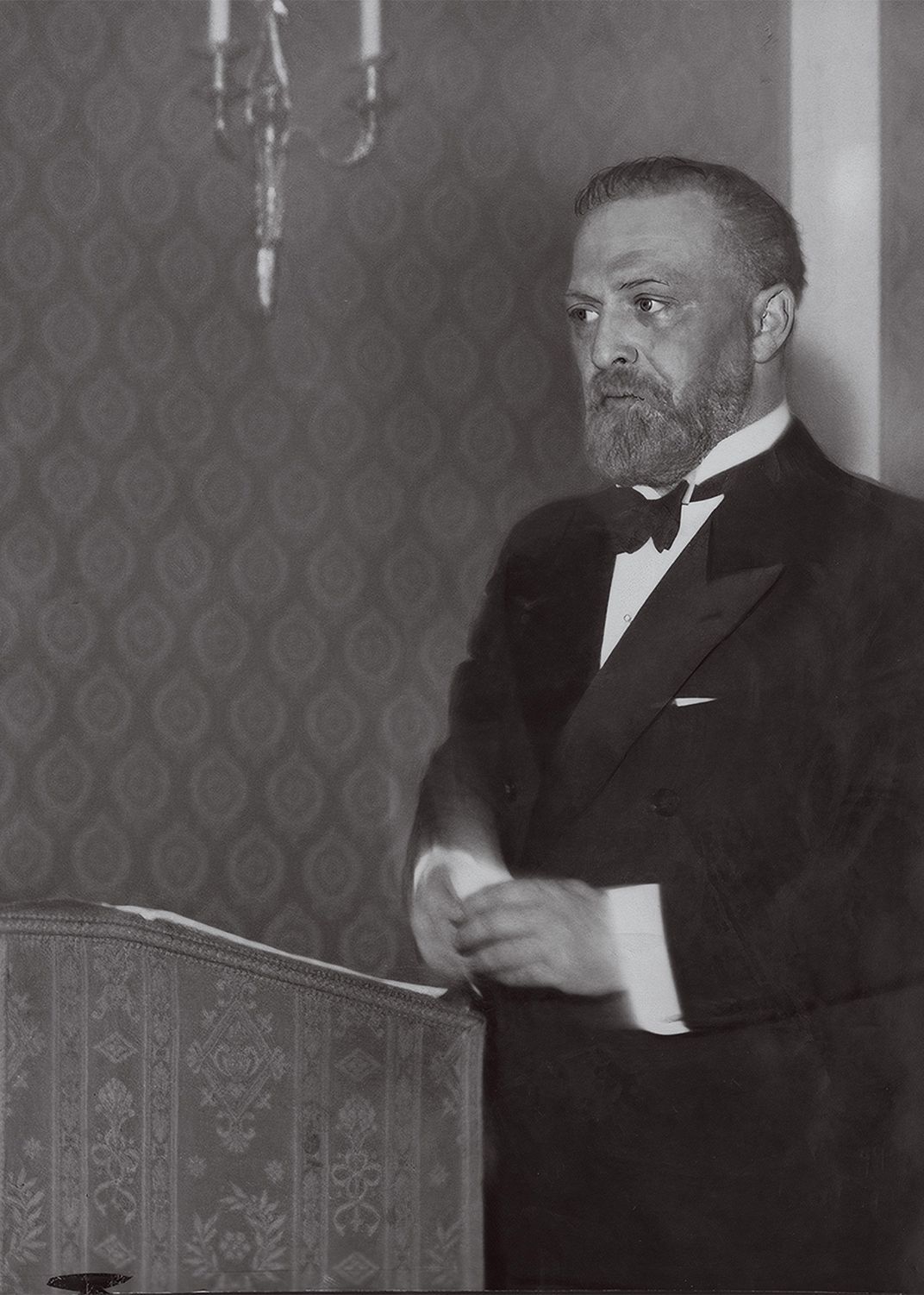 A bearded man in a tuxedo talks at podium