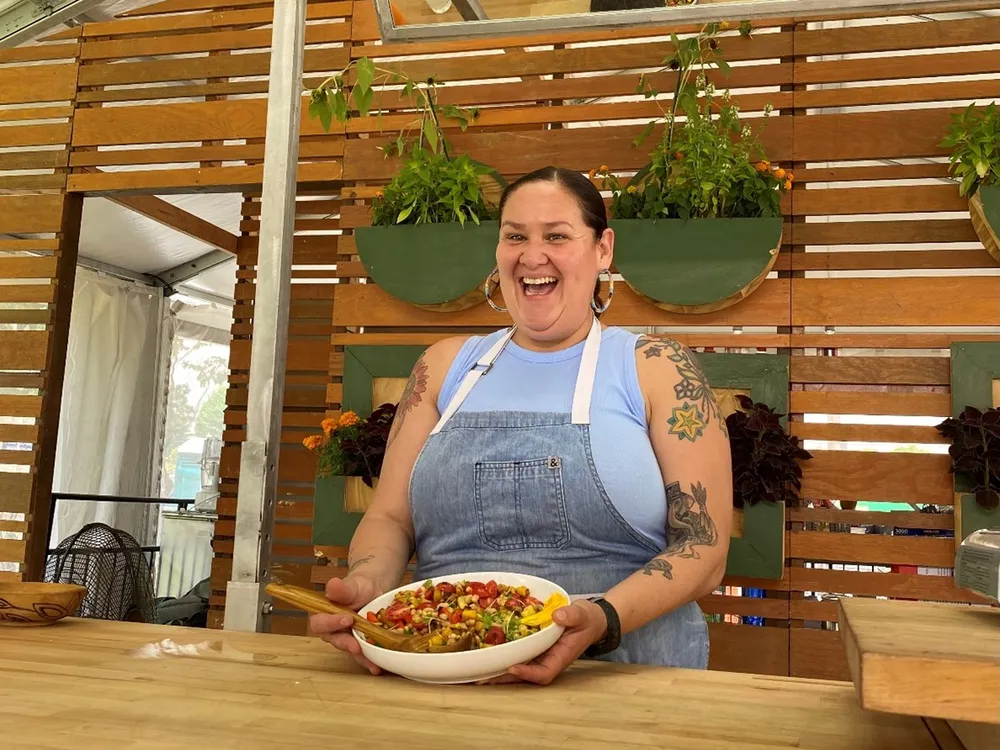 Candid photo of Elena Terry smiling holding a white dish full of colorful beans, peppers, and corn tilted away from her.