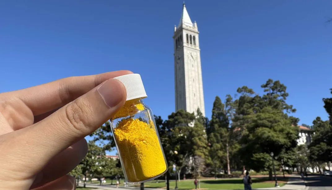 vial of yellow powder in someone's hand in front of a tower