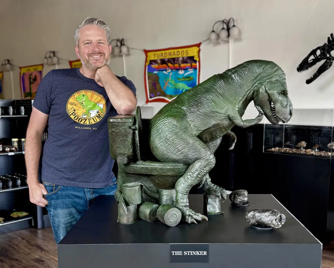 Man with his chin resting on his fist next to a sculpture of a T. rex sitting on a toilet