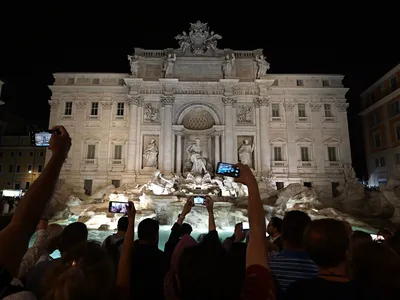 Visitors photograph the Trevi Fountain, which is lit up at night.