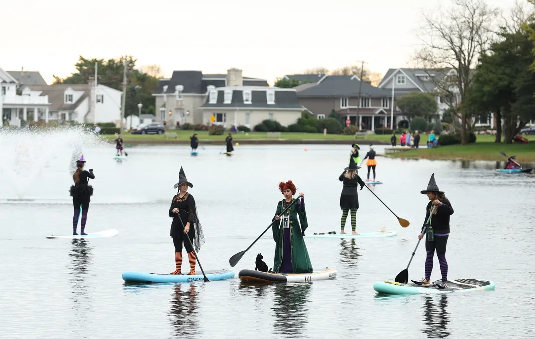 Paddleboarders dressed as witches floating in front of houses