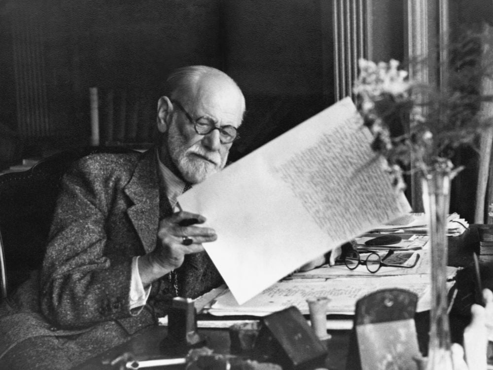 Old man with glasses looking at a piece of paper while sitting at a desk