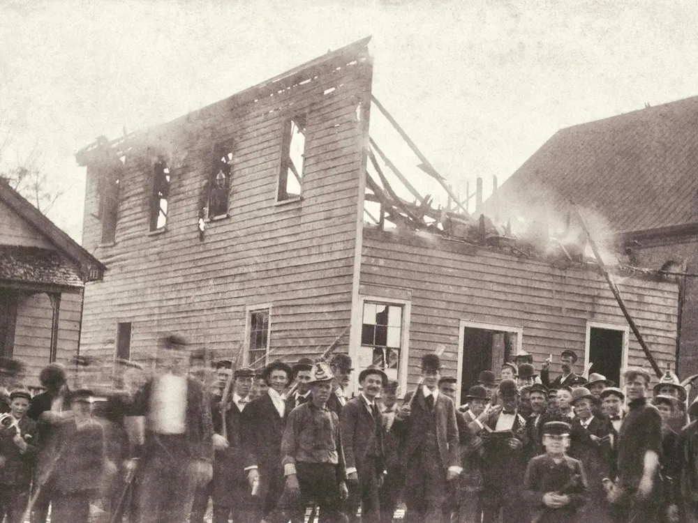 A white mob poses outside of the razed office of the Daily Record, a Black-owned newspaper in Wilmington, North Carolina.