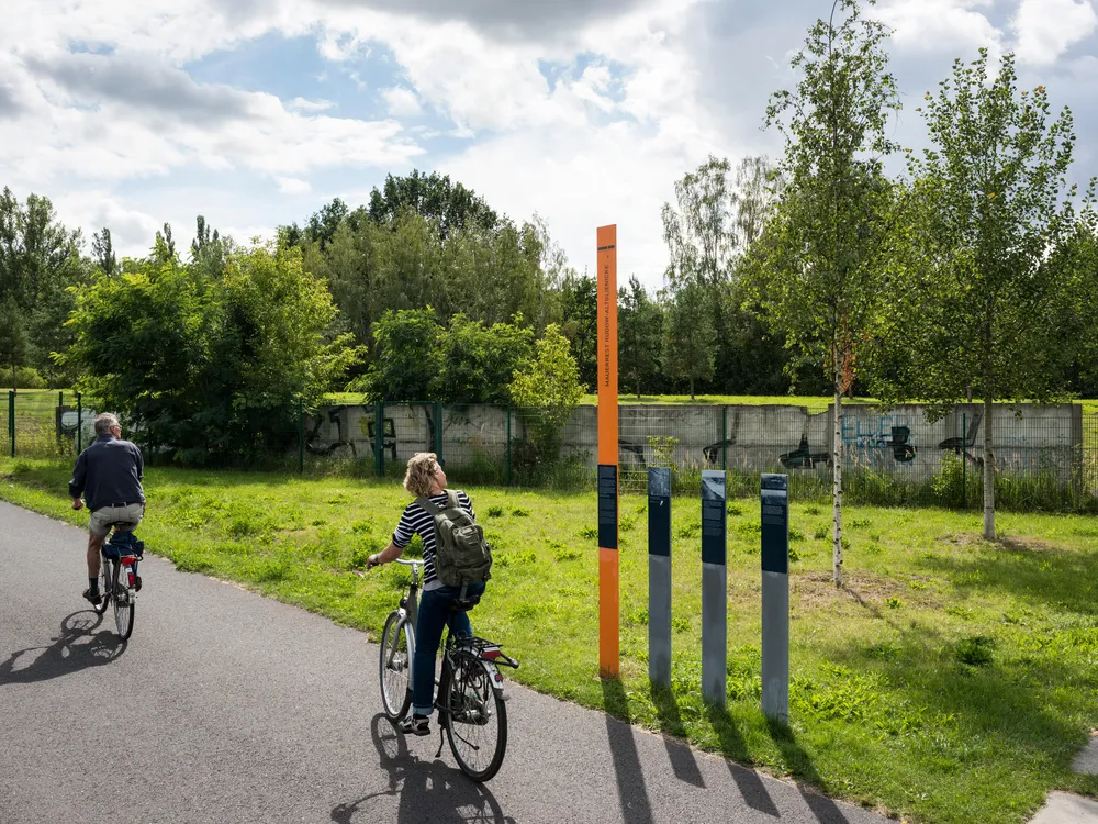 cyclists pass a preserved section of the Berlin Wall