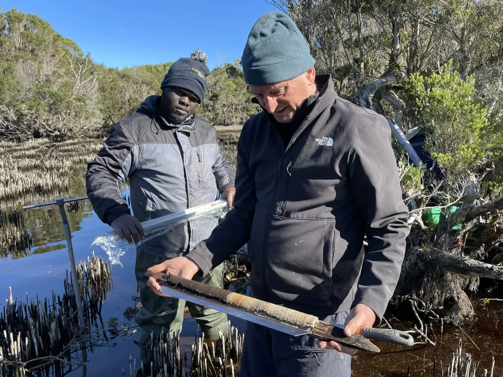 Two scientists study a sediment core in a swamp