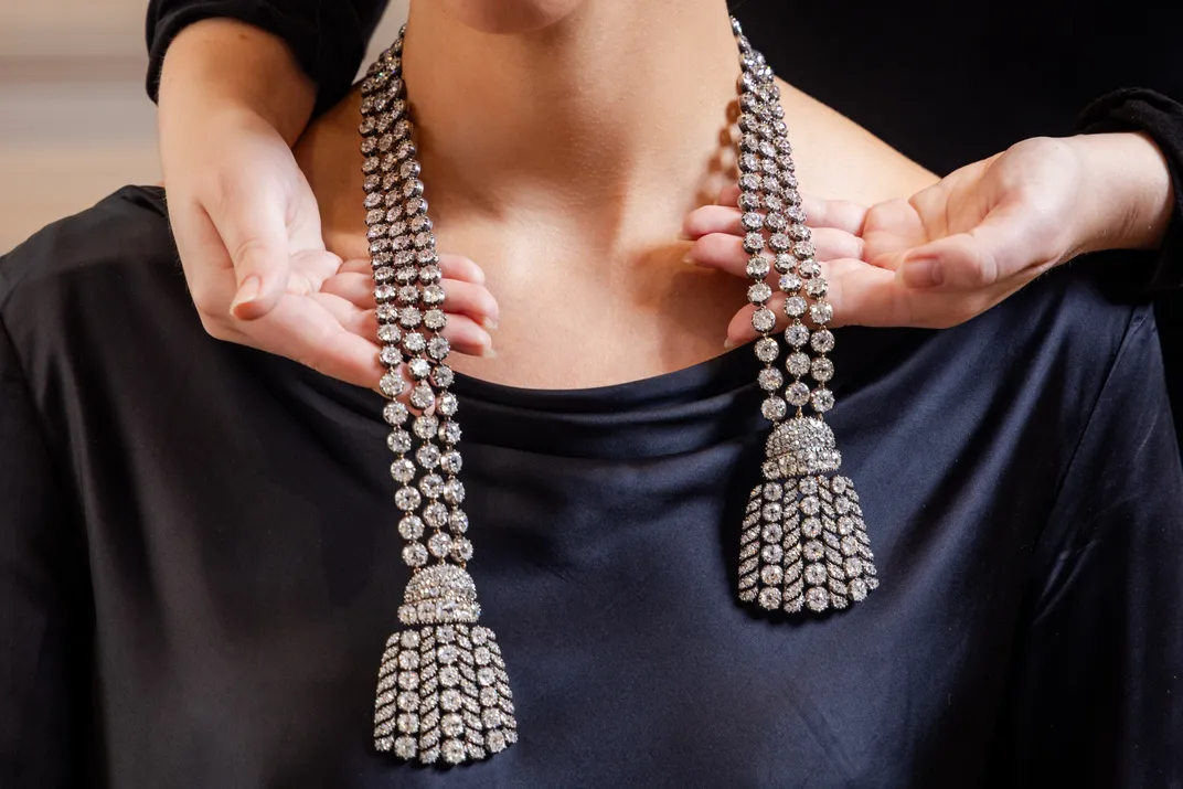 Pair of hands holding up a necklace around a woman's neck